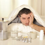 Man with headache and hangover in bed with tablets